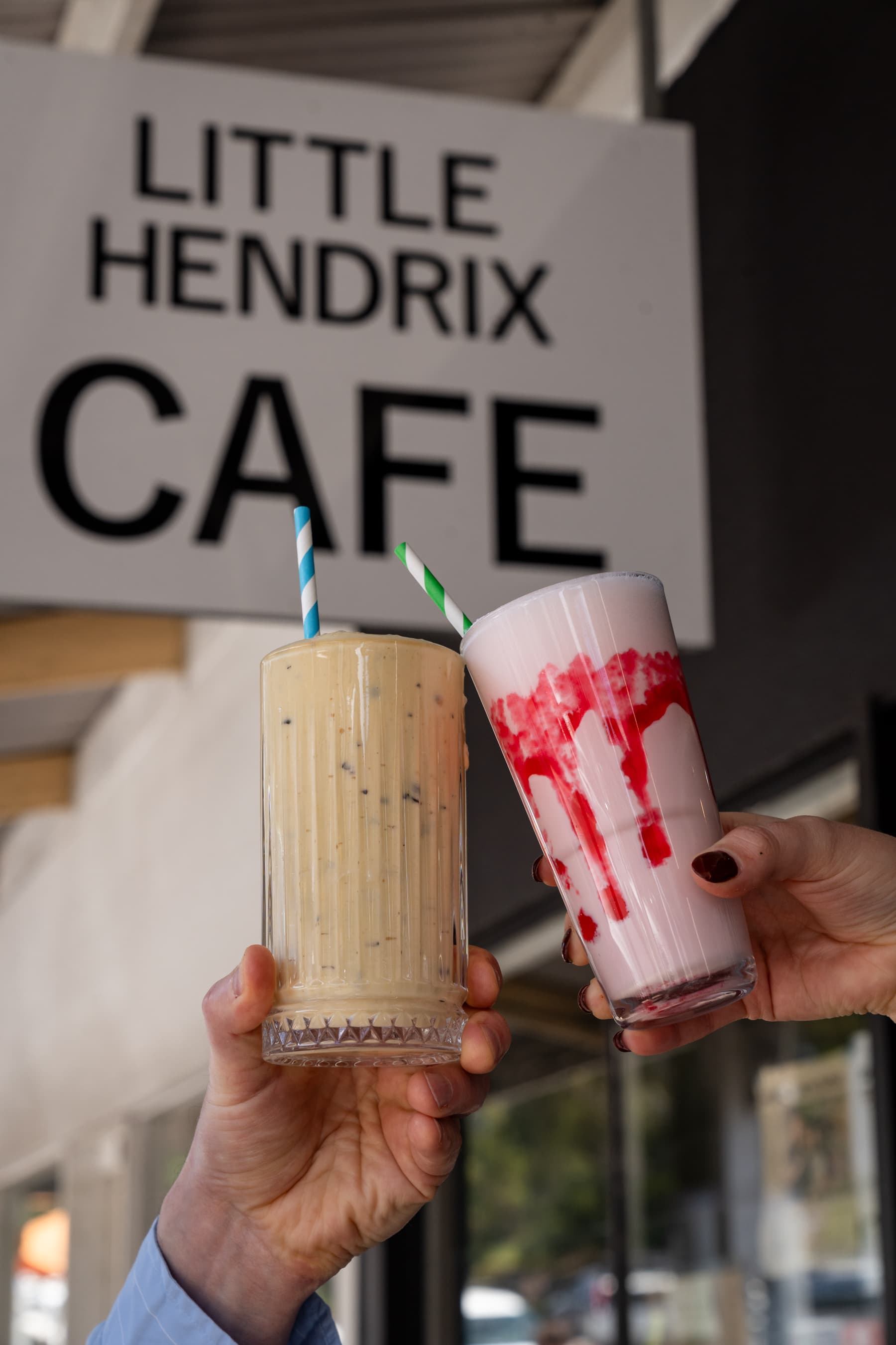 Two Little Hendrix Cafe milkshakes held in front of the cafe sign